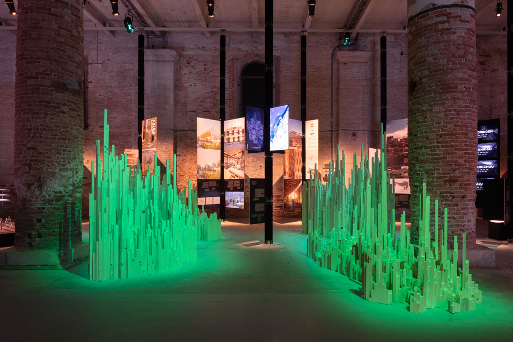 Re-Leaf installation at the Arsenale, with green-lit vertical sculptures and suspended screens between brick columns.